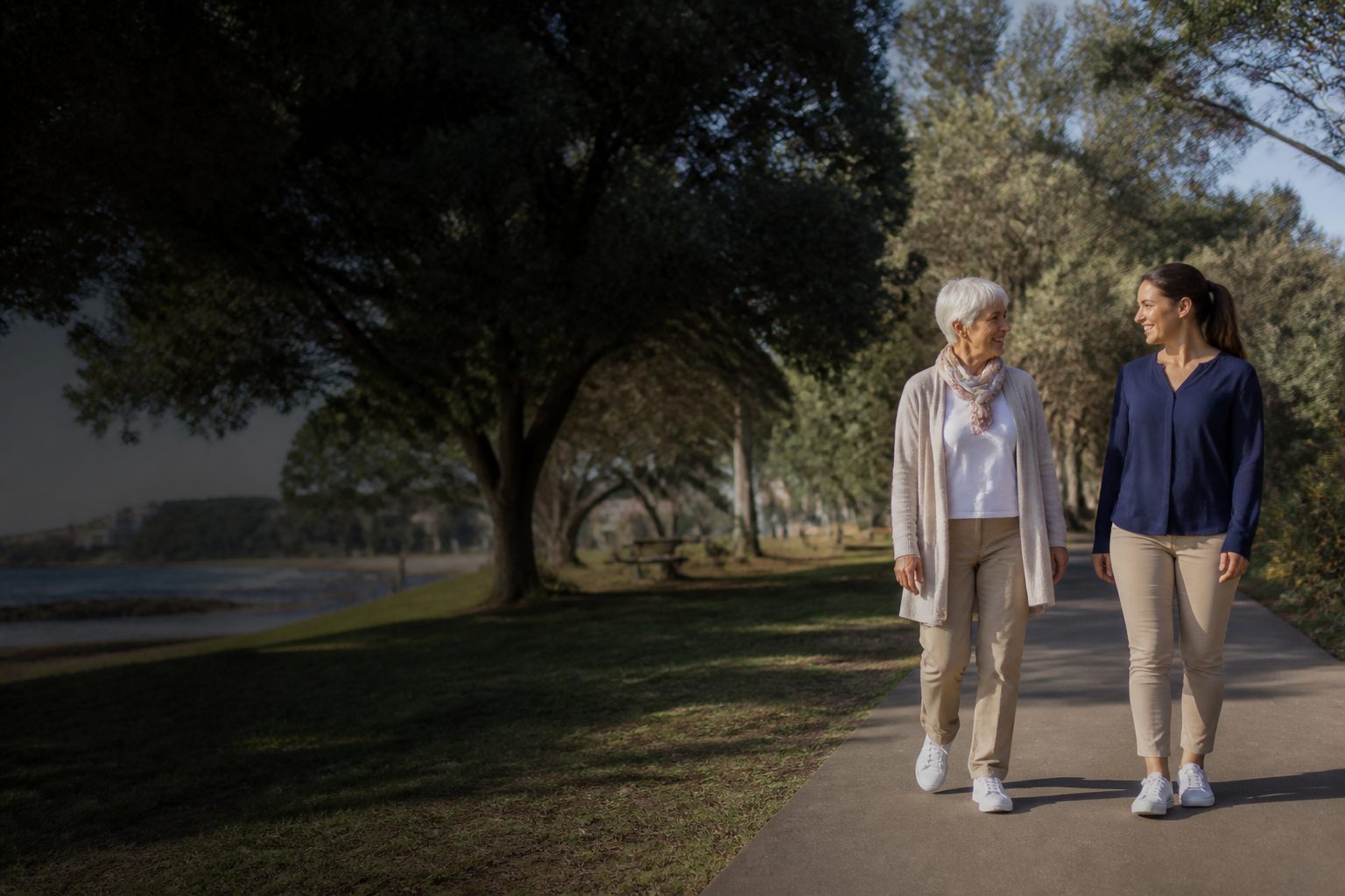 An older woman and support worker enjoying a walk together in a coastal park